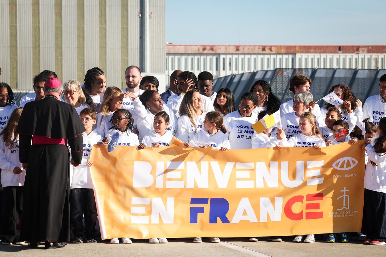 People stand behind a banner reading in French "Welcome to France" as they wait for the arrival of Pope Leo XIV outside Orly Airport, on the outskirts of Paris, on September 25, 2026. (AFP Photo)