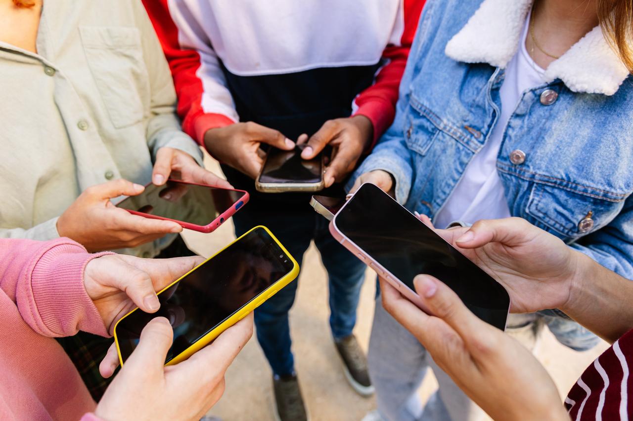 A group of young people hold smartphones together, illustrating social media and mobile technology use among youth. (Adobe Stock Photo)