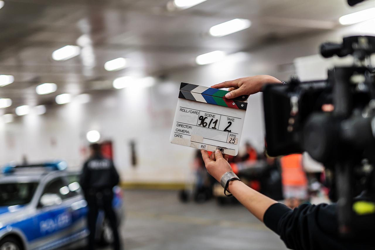 A film crew member holds a clapperboard beside a professional video camera during a production shoot. (Adobe Stock Photo)