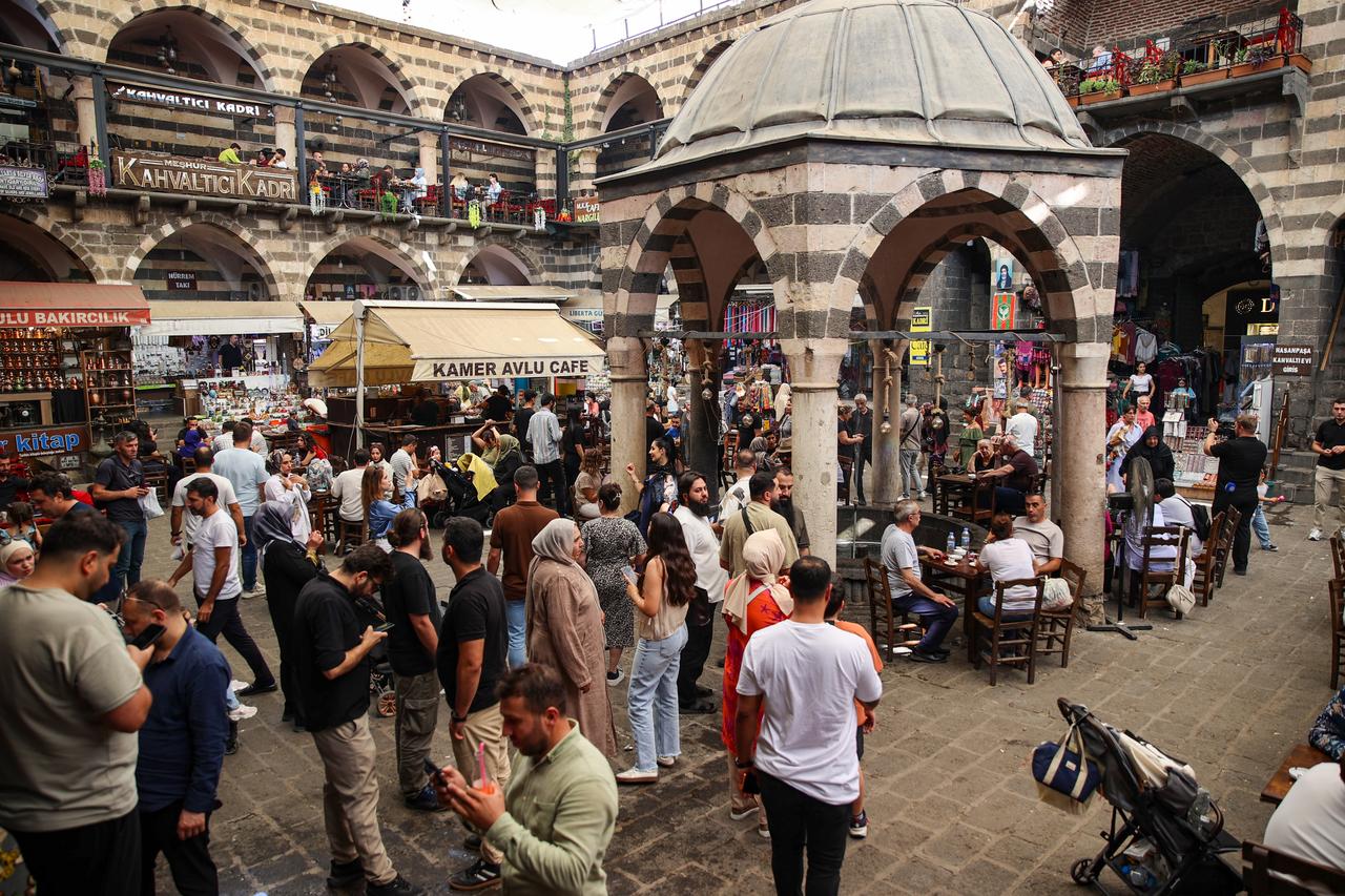 A lively, crowded courtyard in a historic Mardin inn (han), filled with people dining at cafe tables, shopping, and socializing under multi-level stone arcades. (AA Photo)