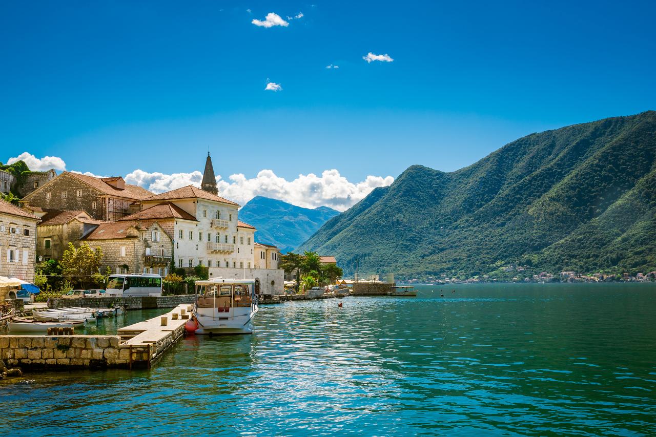 Historic waterfront buildings and boats line the Bay of Kotor in Perast, Montenegro, with mountains rising behind the town. (Adobe Stock Photo)