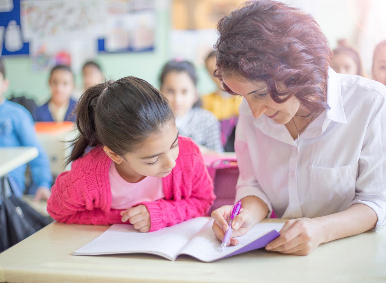A teacher helps a student with schoolwork during a classroom lesson, undated. (Adobe Stock Photo)