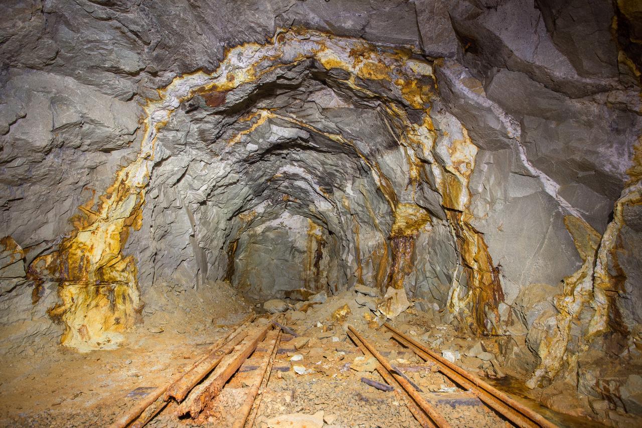 An underground mine tunnel showing exposed mineral-bearing rock formations and old rail tracks. (Adobe Stock Photo)