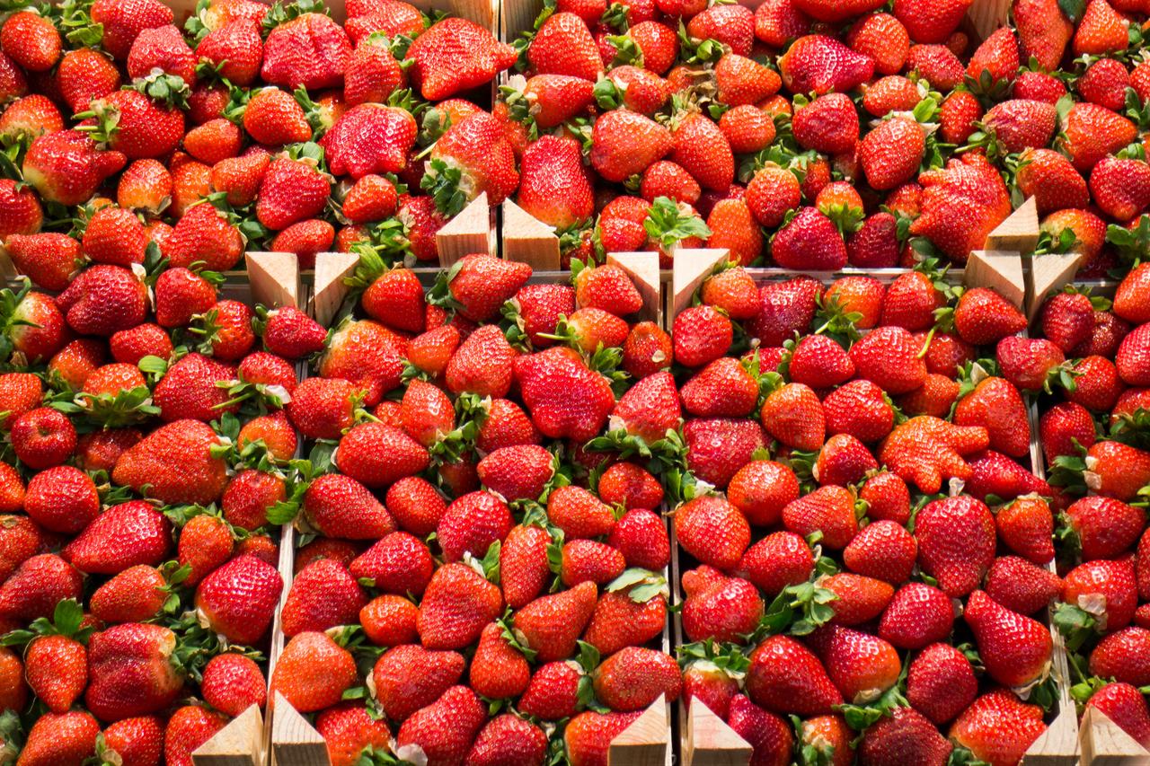 Fresh strawberries are displayed in wooden crates at a market stall, undated. (Adobe Stock Photo)
