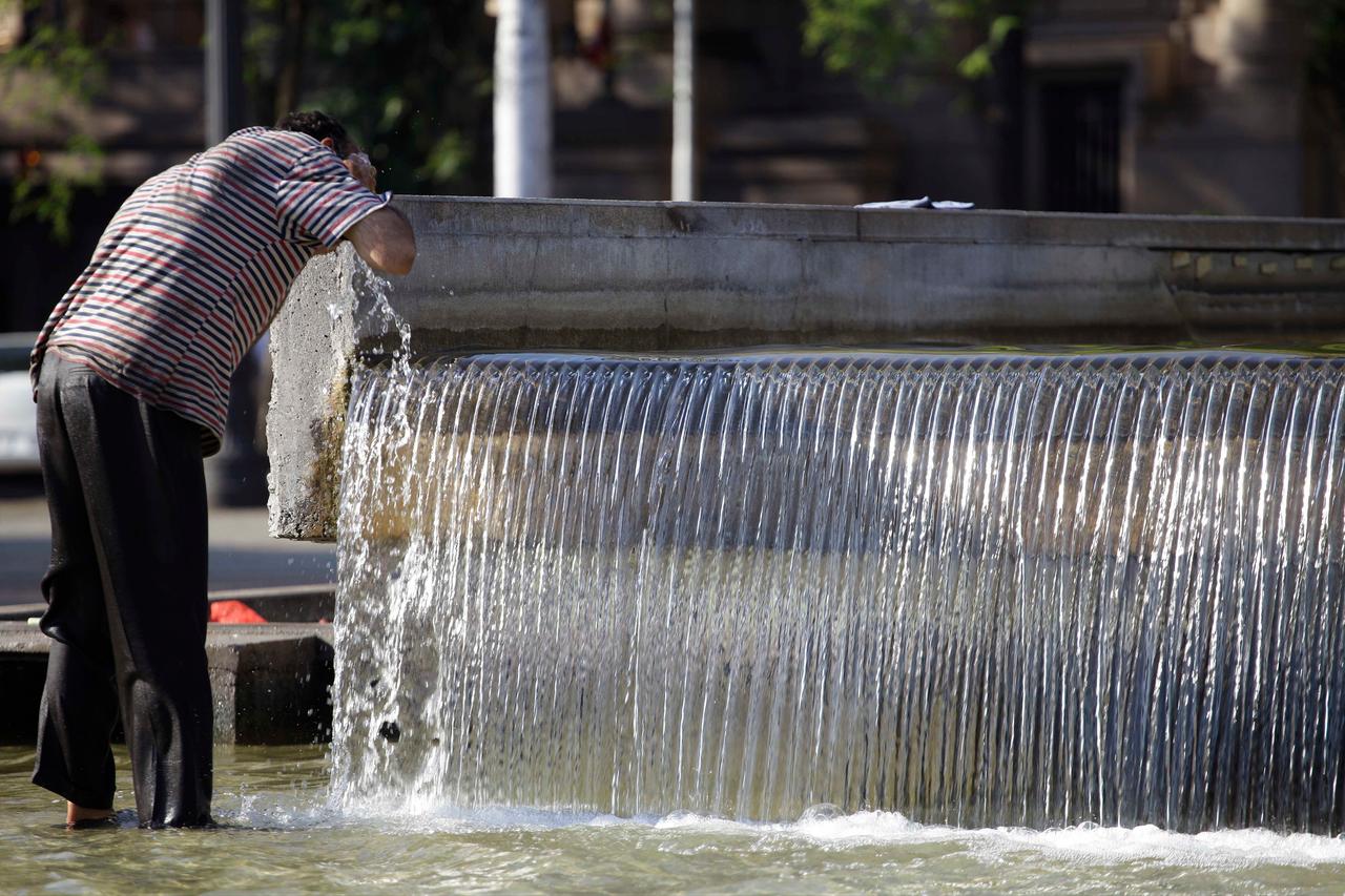 A man cools off with water at a public fountain during hot weather. (Adobe Stock Photo)