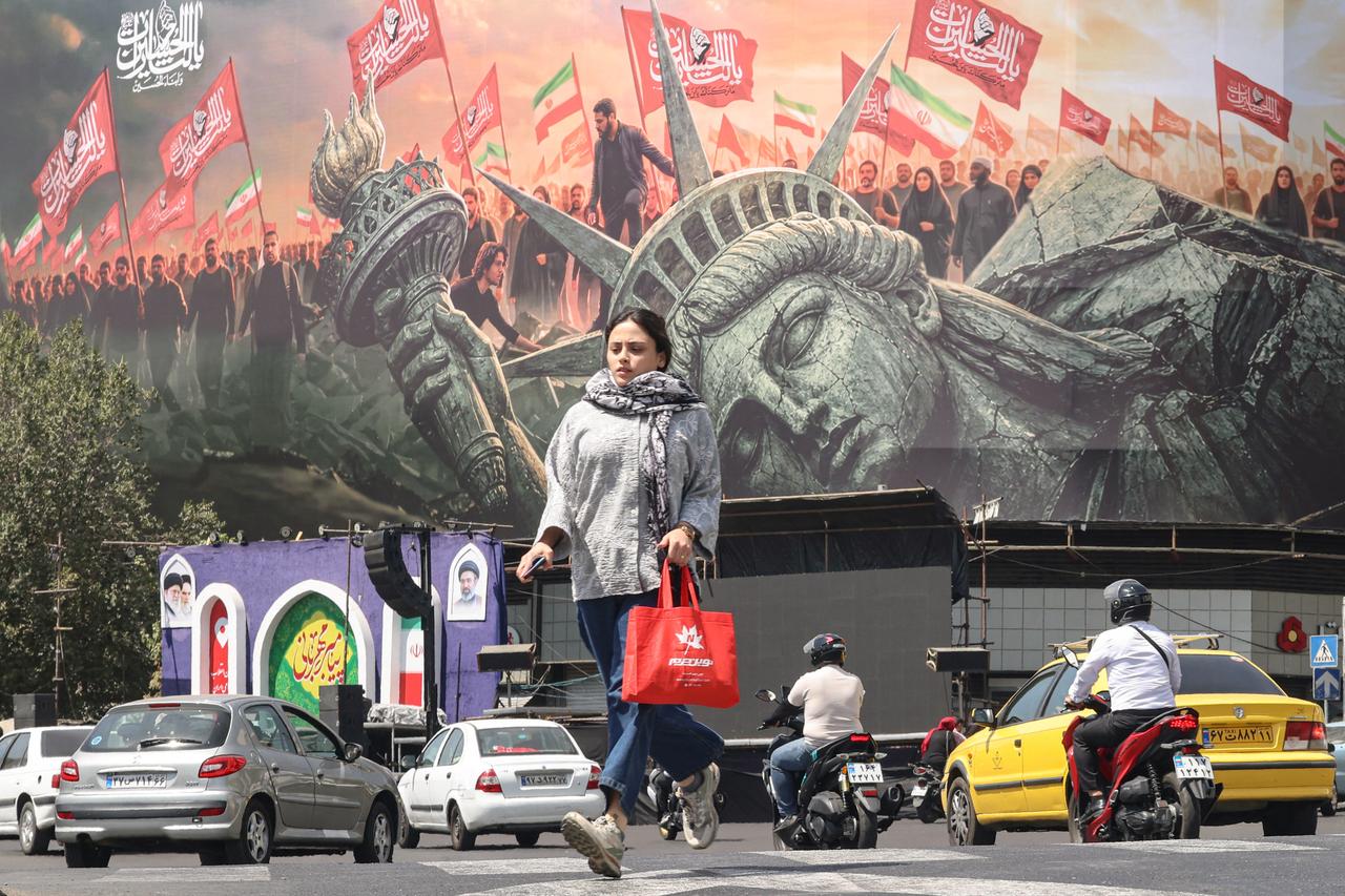 A woman crosses as motorists drive past an anti-US billboard at Enghelab Square in Tehran on September 2, 2026. (AFP Photo)