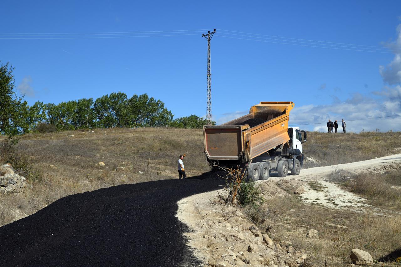 A dump truck lays down a fresh layer of asphalt on the rural dirt road. (AA Photo)