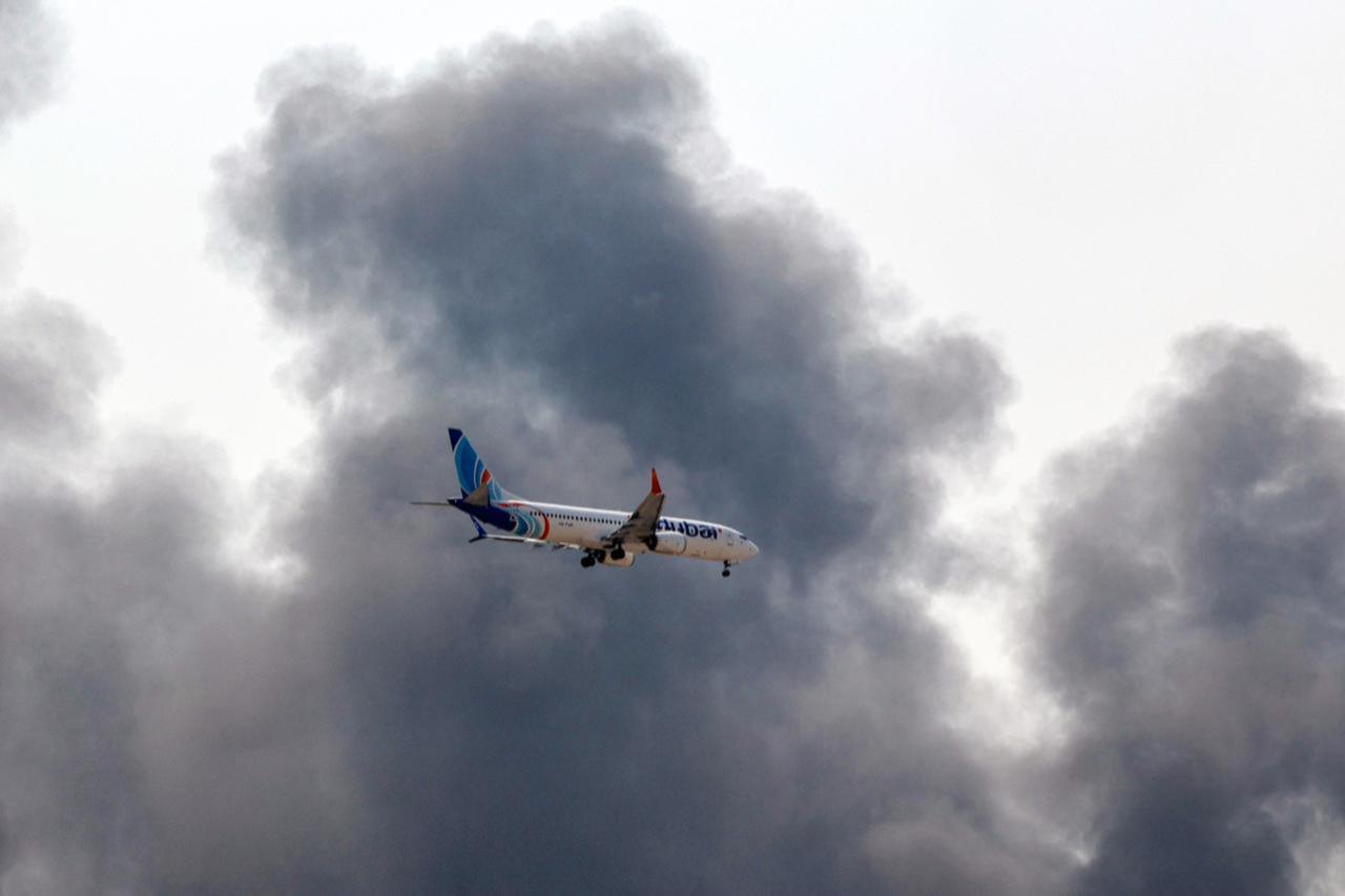 A Flydubai Boeing 737 Max aircraft prepares for landing as a smoke plume rises from an ongoing fire near Dubai International Airport in Dubai on March 16, 2026. (AFP Photo)