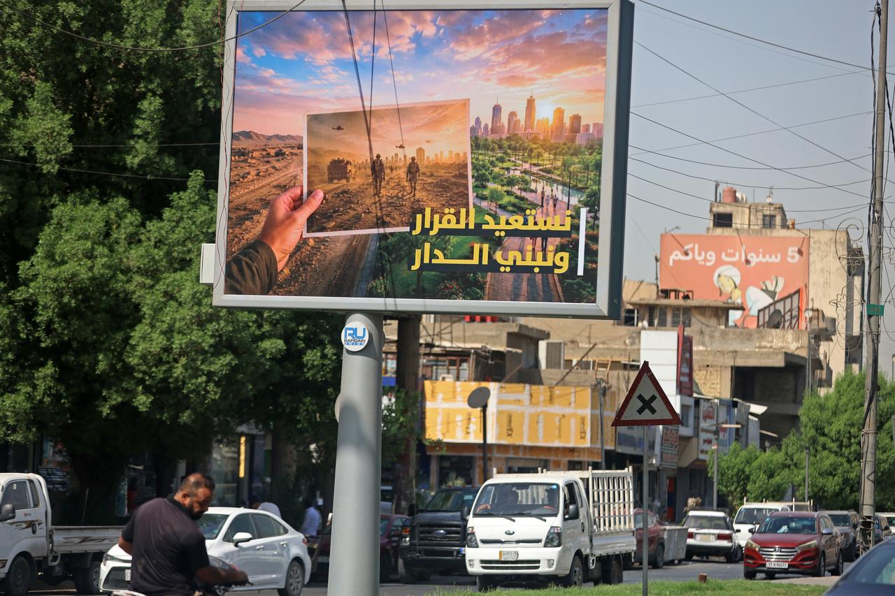 Vehicles drive past a billboard carrying the Arabic slogan 'Reclaiming the decision and building the home', at the Saadoun Square in Baghdad on September 29, 2026. (AFP Photo)