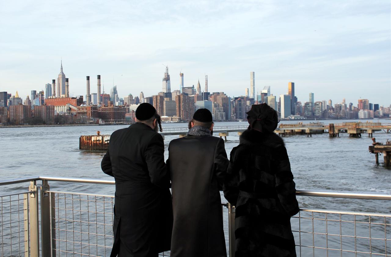 Three people dressed in black look across the East River toward the Manhattan skyline in New York City. (Adobe Stock Photo)