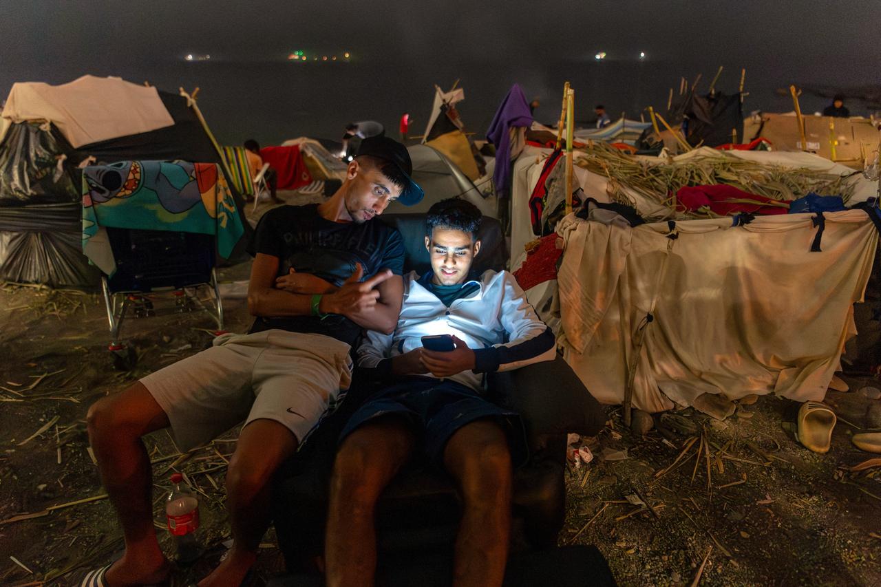 Two migrants use a smartphone as they spend the night next to makeshift shelters on El Trampolin beach in Ceuta on September 1, 2026. (AFP Photo)