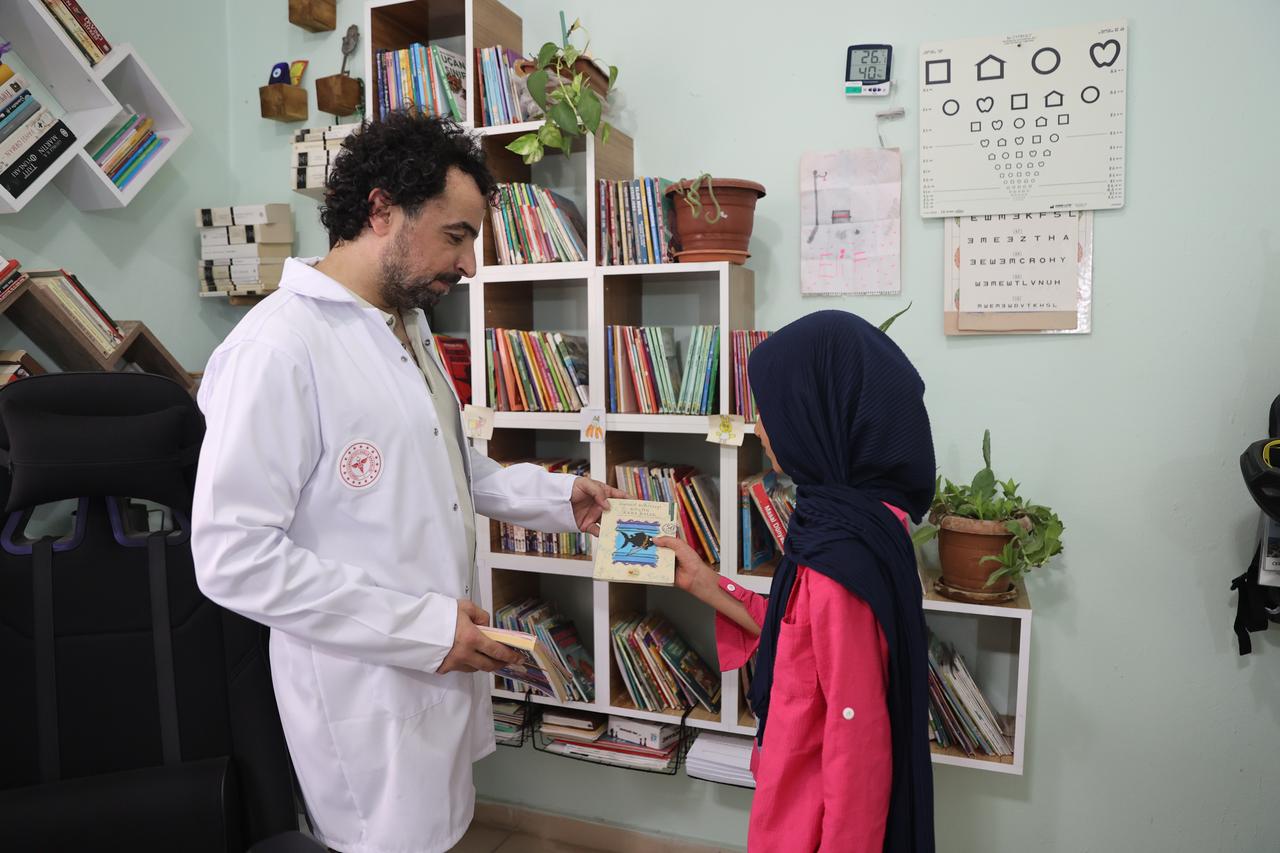 Family physician Selman Yasar handing a book to a girl in his office. (AA Photo)