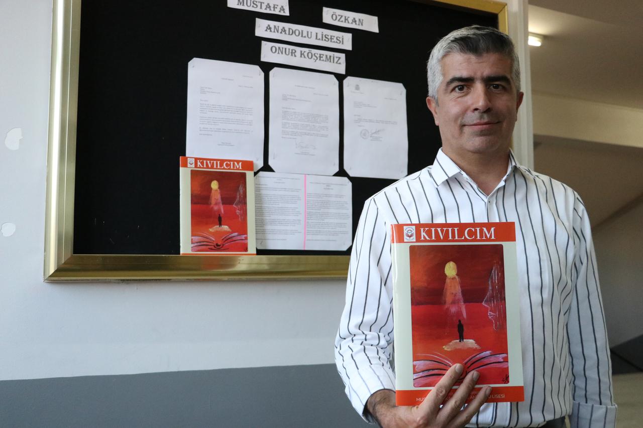 Mustafa Ozkan Anatolian High School Principal Fatih Sahin holds an issue of the school's Kivilcim literary magazine in front of a display featuring letters received by the school in Kayseri, Türkiye. (AA Photo)