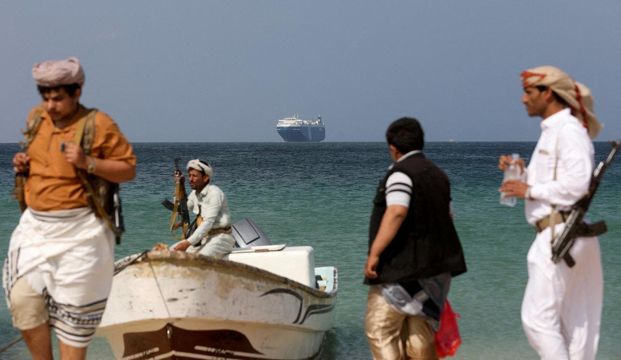 Armed men stand on the beach as the Galaxy Leader commercial ship, seized by Yemen's Houthis last month, is anchored off the coast of al-Salif, Yemen, Dec. 5, 2023, Reuters